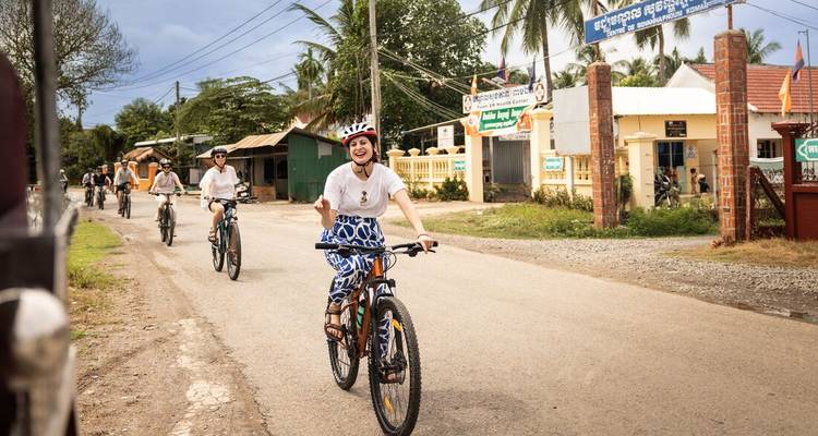 Groupe de cyclistes dans une zone rurale avec des panneaux en langue cambodgienne.