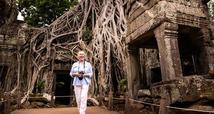 Femme souriante devant des ruines de temple enlacées par des racines d'arbres.