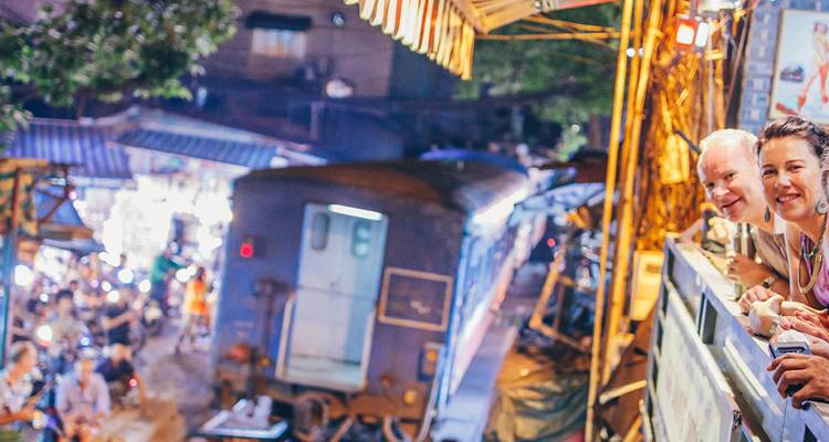 Turistas observando mientras un tren pasa por una calle concurrida de noche.