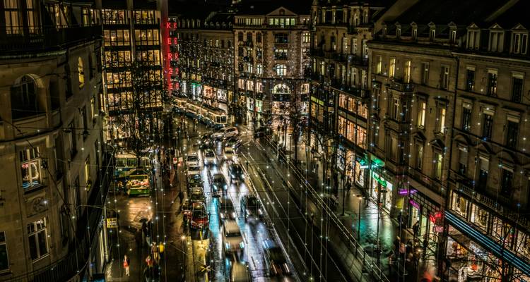 Paysage urbain nocturne avec bâtiments illuminés et circulation routière.