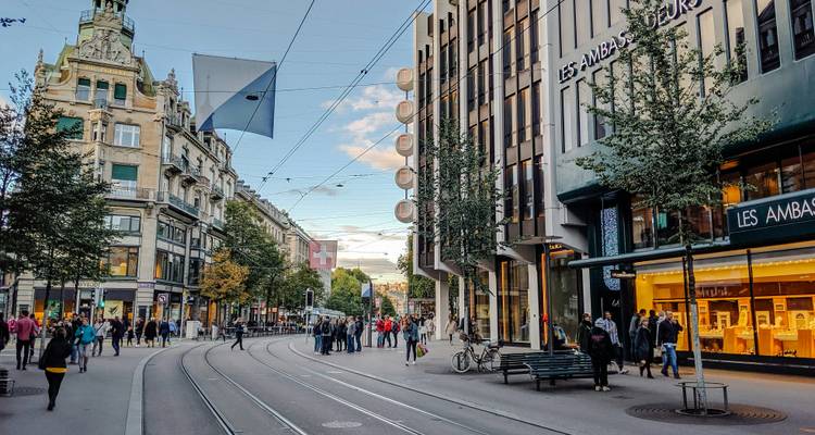 Scène de rue animée dans une zone urbaine avec des magasins et des gens.