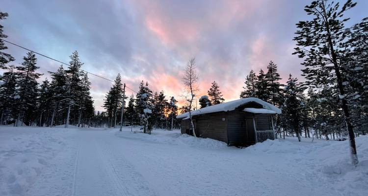 Chalet couvert de neige avec un ciel de coucher de soleil en arrière-plan.