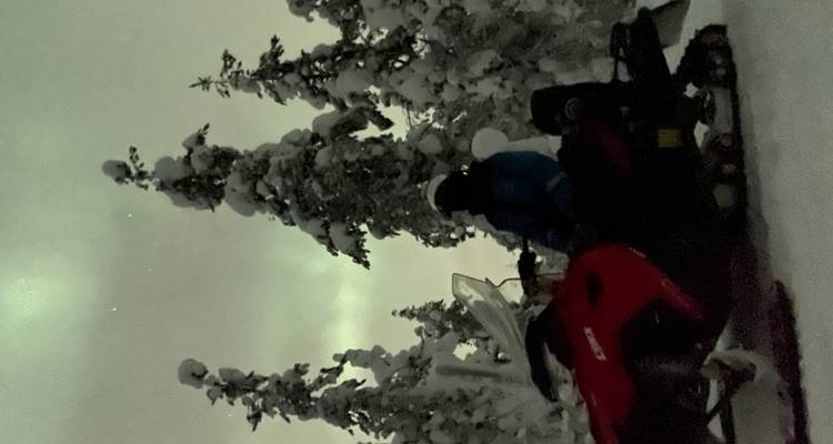 Motoneige sous les aurores boréales dans une forêt enneigée.
