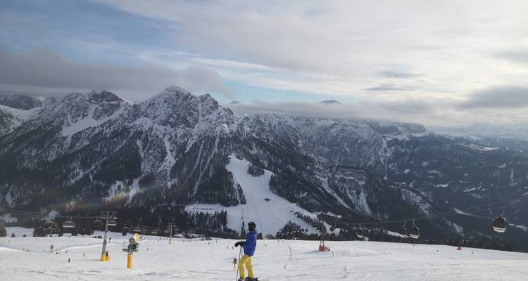Skieur sur une pente enneigée avec téléphériques dans une chaîne de montagnes enneigées.