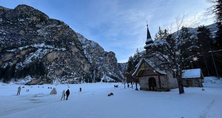 Église couverte de neige avec montagnes et lac, personnes qui marchent.
