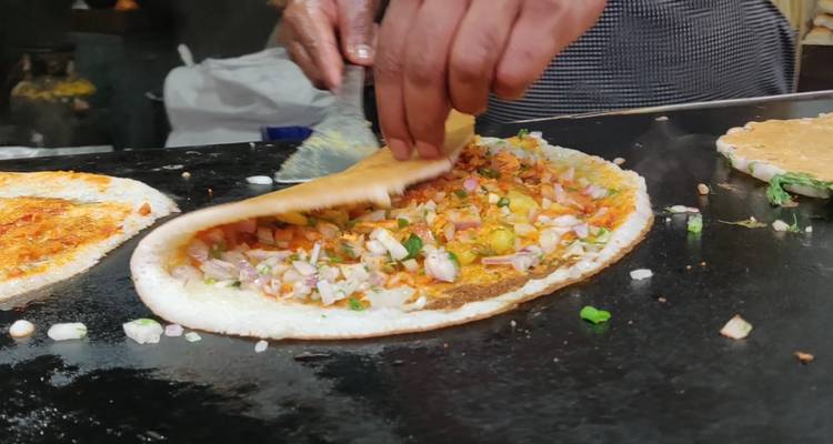Nahaufnahme von Händen, die ein gefülltes Dosa auf einer heißen Grillplatte an einem Straßenverkaufsstand zubereiten