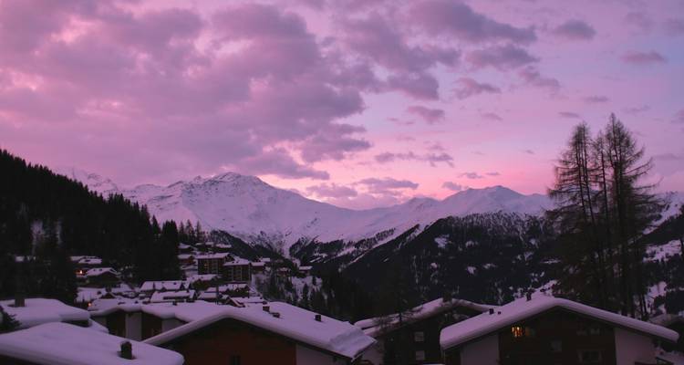 Village enneigé avec un ciel rose au coucher du soleil.