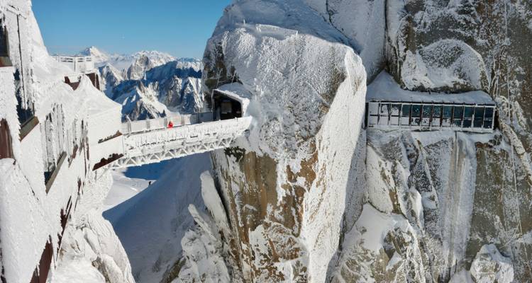 Pont suspendu au-dessus d'une falaise enneigée.