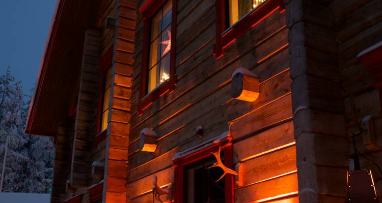 Extérieur éclairé d'une cabane aux murs lambrissés de bois la nuit.