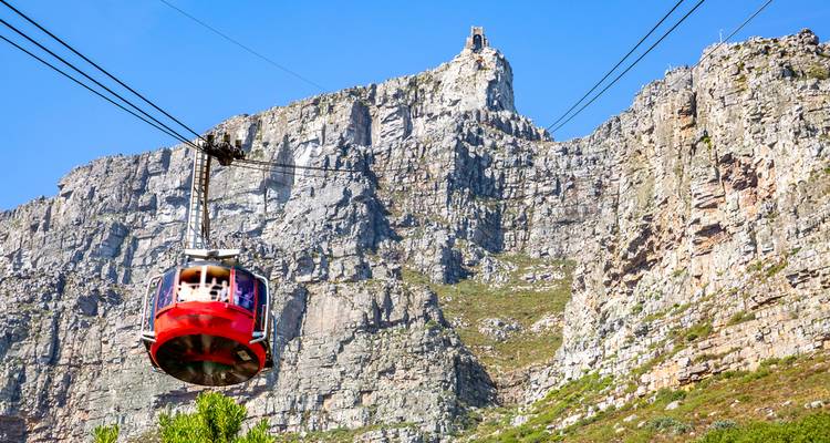 Un teleférico colorido asciende por los acantilados escarpados de la Montaña de la Mesa en un día de cielo azul brillante.