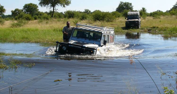 Véhicule de safari traversant l'eau dans la nature sauvage.