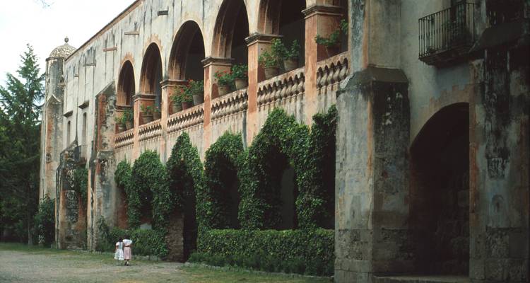 Bâtiment colonial historique avec balcons voûtés et lierre.
