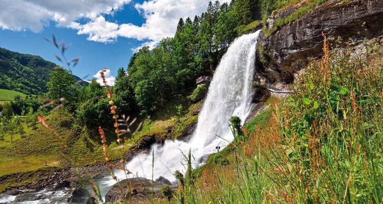 Ein majestätischer Wasserfall, der über üppige grüne Hügel unter einem klaren blauen Himmel herabstürzt.