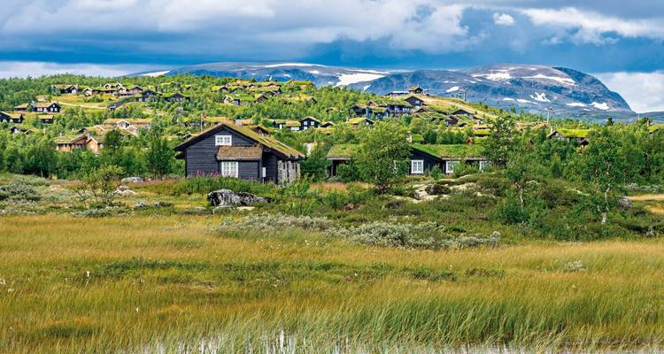 Traditionelle Holzhäuser vor einer Kulisse aus weiten Hügeln und blauem Himmel.