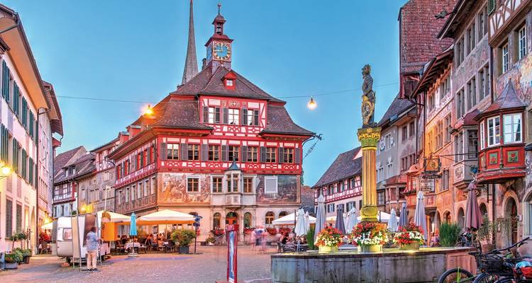 Place de ville historique avec une fontaine décorée et des bâtiments traditionnels.