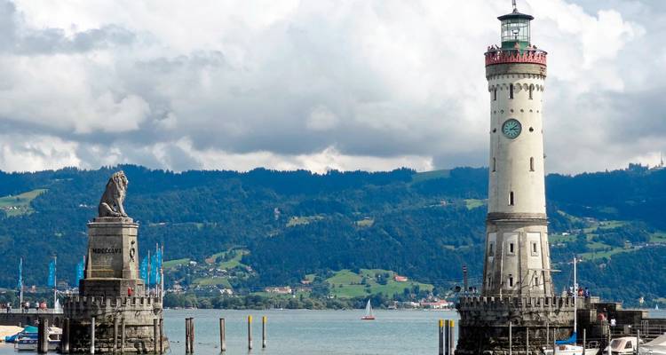 Phare et statue de lion à l'entrée d'un port, avec des montagnes en arrière-plan.