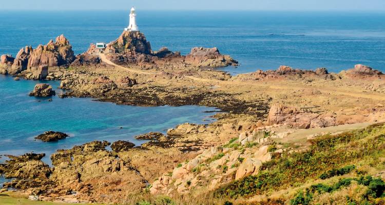 Lighthouse on rocky coast with clear blue sea.