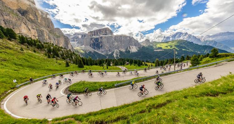 Cyclists on a mountain road with rocky peaks in the background.