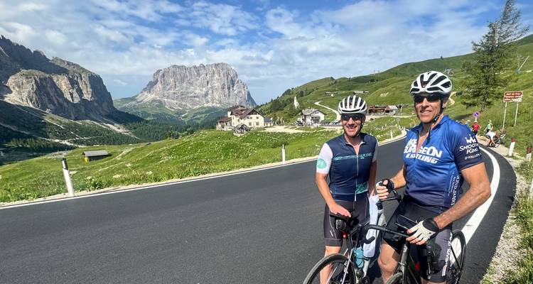 Two cyclists with road and mountain scenery.