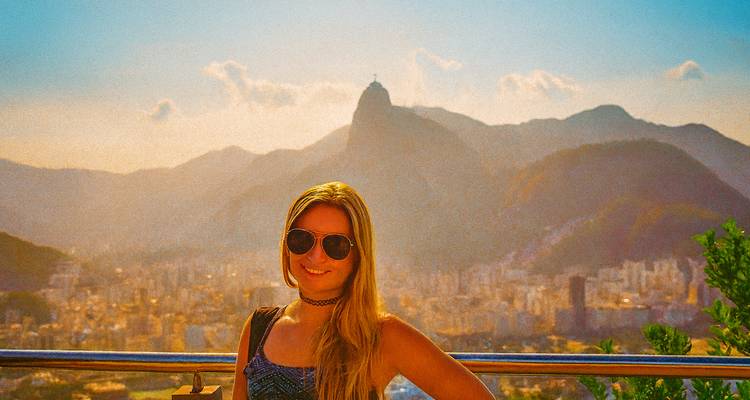Person posing with a cityscape and mountain in the background at sunset.