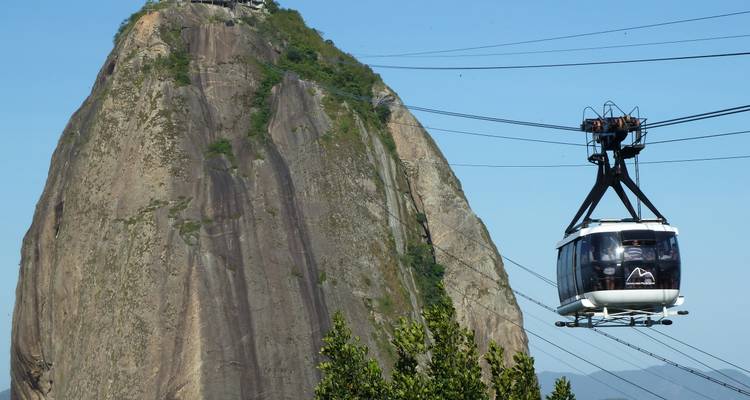 Zahnradbahn, die an dem Felsmonolith des Zuckerhuts vorbei unter klarem Himmel aufsteigt.