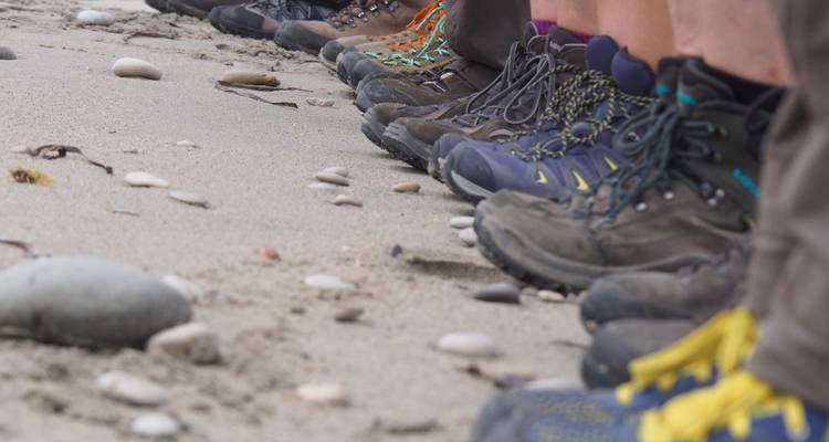 Row of hiking boots on a sandy beach.