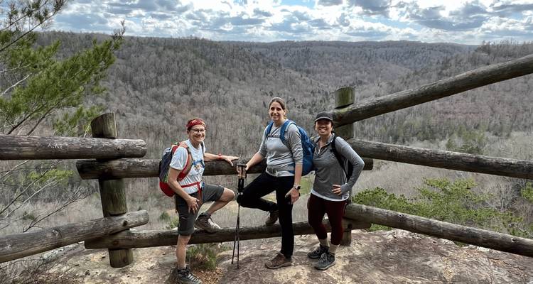 Trois randonneurs posant à un point de vue avec une vue étendue sur la forêt.