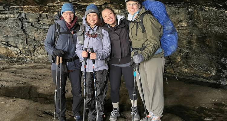 Quatre randonneurs en vêtements chauds posant à l'intérieur d'une grotte rocheuse.