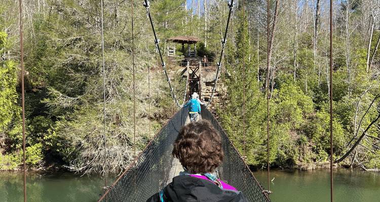 Deux personnes marchant sur un pont suspendu au-dessus d'une rivière.