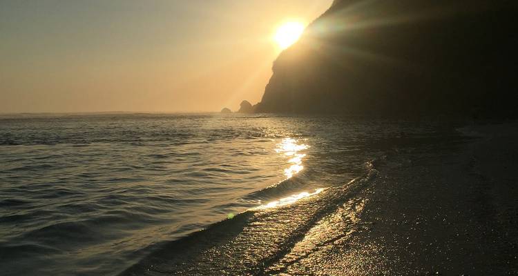 Sonnenuntergang über einem Strand mit Wellen, die sanft an das Ufer plätschern.