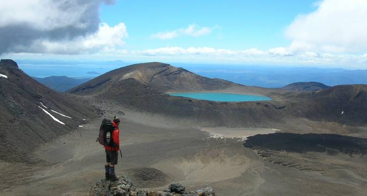 Un excursionista con vistas a un paisaje volcánico con un lago azul.