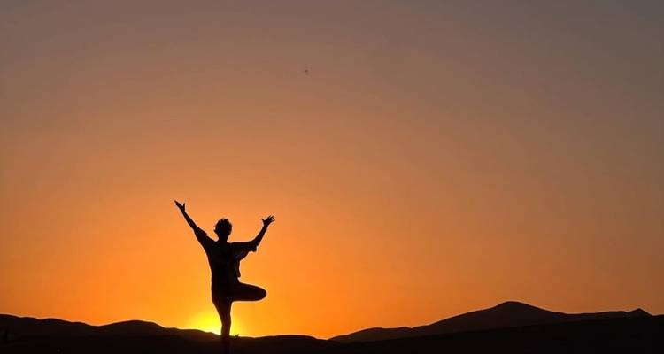 Silhouet van een persoon in yoga houding bij zonsondergang.