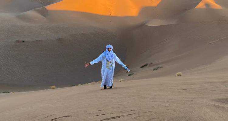 Persoon in traditionele kleding lopend in zandduinen.