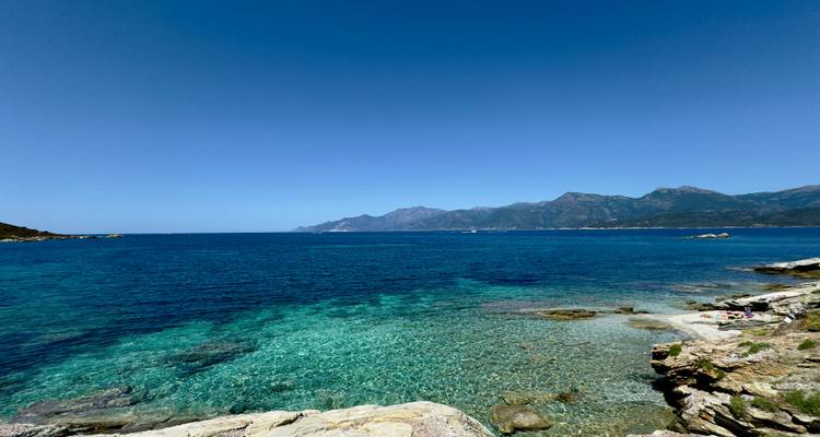 Mer turquoise avec fond de montagne sous un ciel bleu clair.