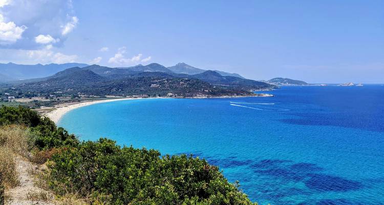 Plage immense avec un océan bleu vif et des montagnes lointaines.