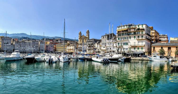 Une marina avec des bateaux et des bâtiments colorés reflétés dans l'eau.