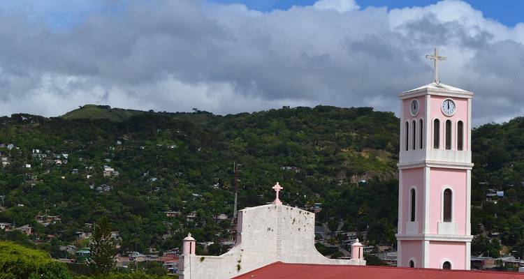 Pink church bell tower with lush hills in the background.