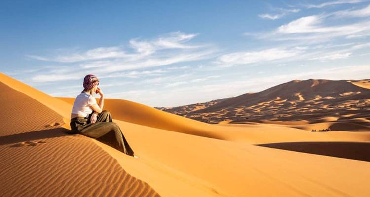 Une personne assise sur des dunes de sable pendant la journée.