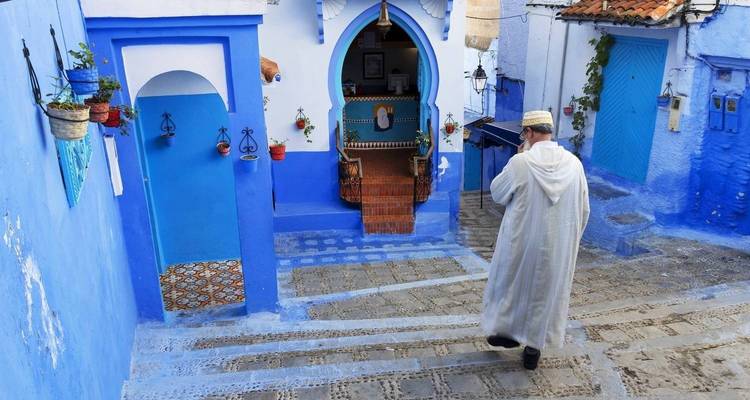 Personne en tenue traditionnelle marchant dans une rue peinte en bleu.