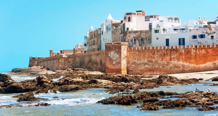Una ciudad costera fortificada con rocas arenosas y cielos azules.