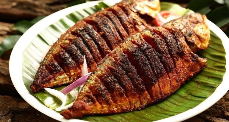 Deux filets de poisson grillés sur une feuille de bananier, garnis d'oignons.