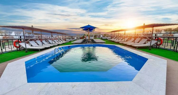 Piscine sur une terrasse avec chaises et parasols sous un ciel bleu.