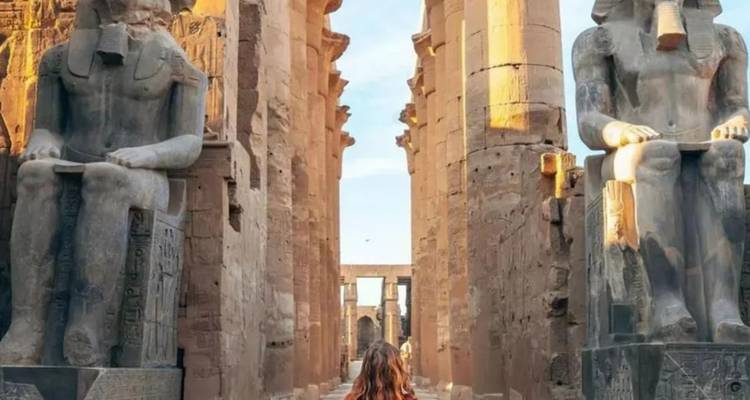 Ruines d'un temple antique avec de grandes statues et une personne marchant entre les colonnes.