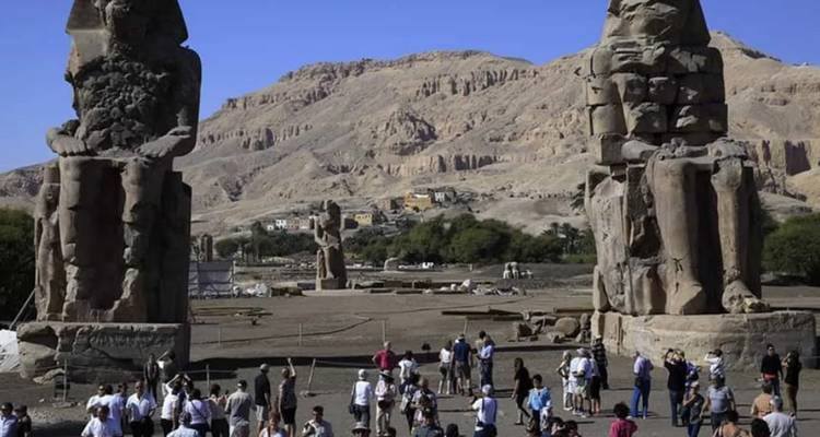 Statues anciennes et touristes dans un espace ouvert avec des collines en arrière-plan.