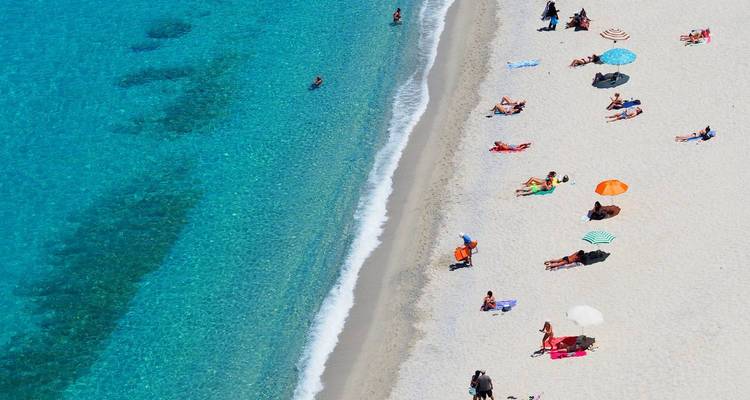 Aerial view of a beach with people sunbathing and umbrellas.