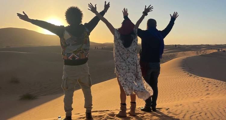 Trois amis levant les bras au coucher du soleil dans le désert.
