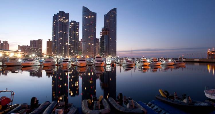 Vista del puerto con modernos rascacielos y barcos amarrados durante el crepúsculo.