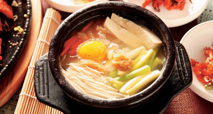 Guiso tradicional coreano en una olla negra, rodeado de guarniciones.