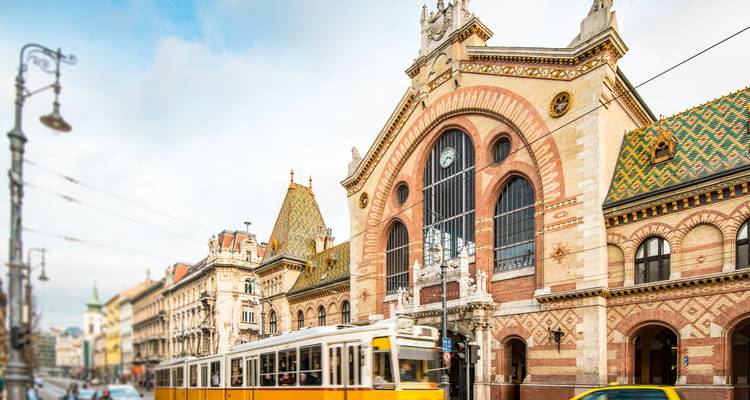 Halle de marché historique avec tramway passant devant.
