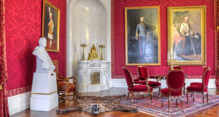 Intérieur luxueux avec des chaises rouges et des portraits historiques.